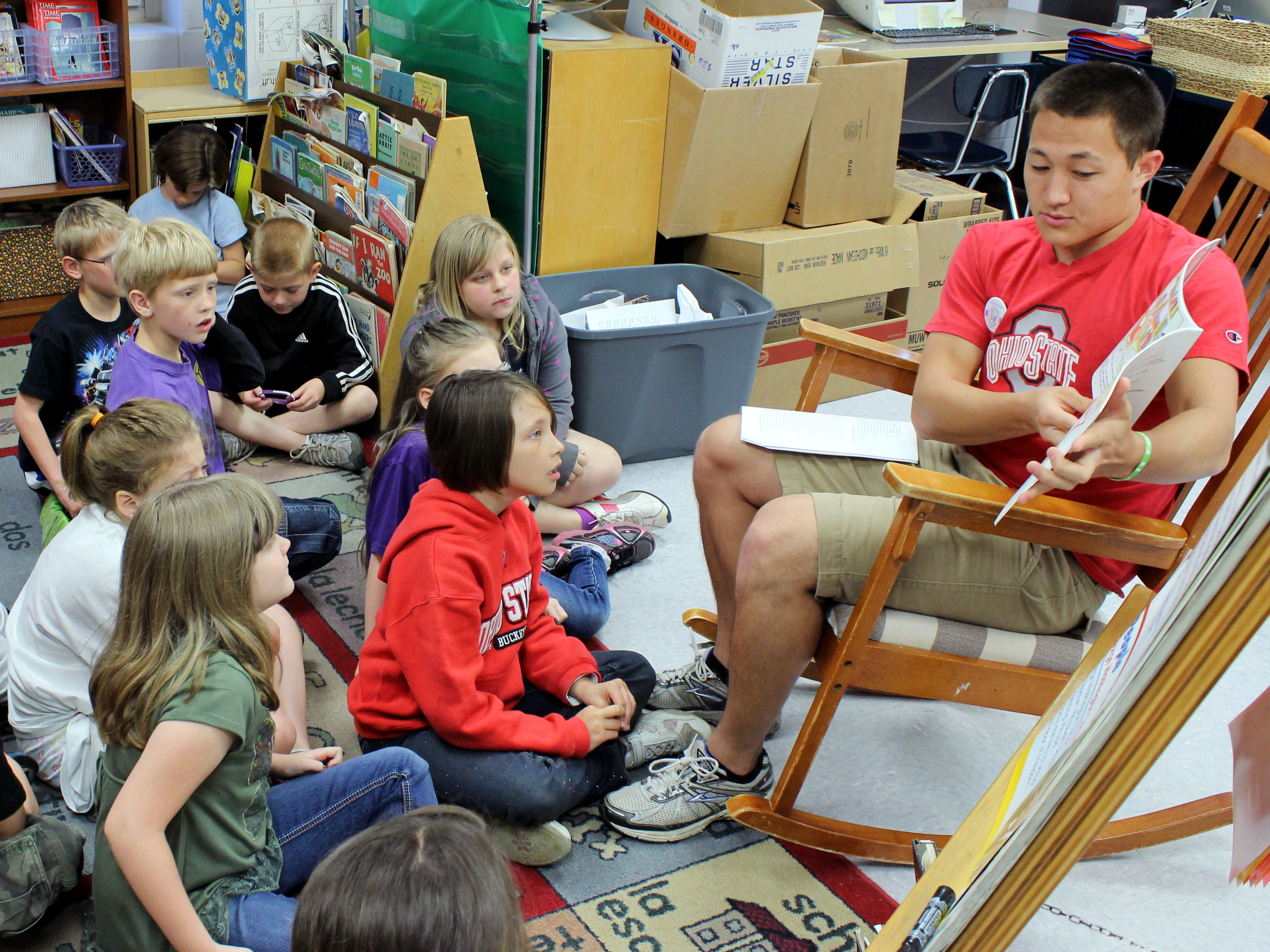 A college student reading to a group of young children.